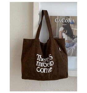 Close-up of brown textured canvas tote bag featuring white artistic lettering and side tag