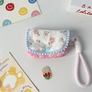 Detailed close-up of pink quilted floral coin purse with blue pom-pom trim and woven strap