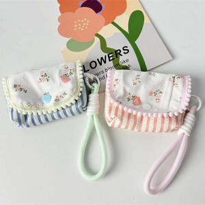 Close-up of floral quilted small storage pouch with decorative pompoms and strap