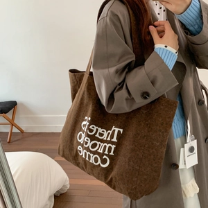 Brown corduroy tote bag with white letter print shown worn by a model in daily life