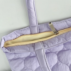 Detail der hellvioletten Stepptasche mit silbernem Reißverschluss und weicher Textur