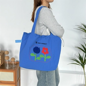 Detailansicht der blauen Kordelzug-Einkaufstasche mit Blumenstickerei und Schriftzug