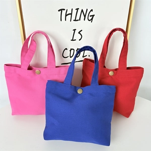 Detail of canvas tote bags showing secure brass snap button closure in multiple colors