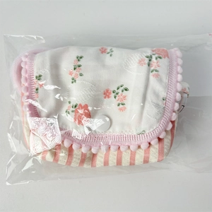 Detailed view of floral striped quilted pouch with pink pom-poms in protective packaging