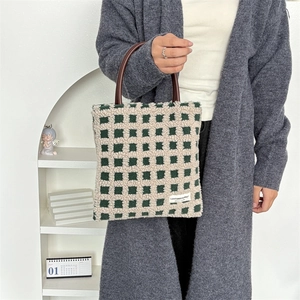 Détail du cabas en peluche à damier vert avec poignée en cuir et étiquette logo