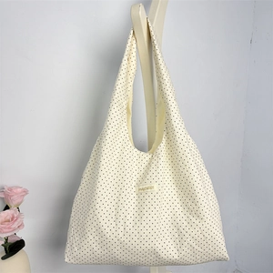 Detail of polka dot canvas tote bag featuring a brand label on white wall hook
