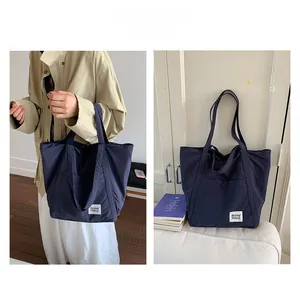 Detail of deep blue nylon tote bag featuring a white minimalist brand patch and long straps