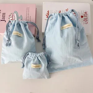 Three light blue cotton linen drawstring storage bags in various sizes on a pink book