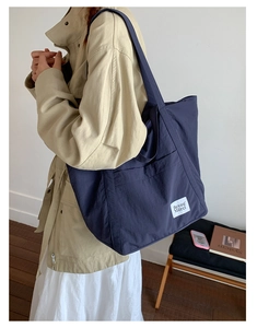 Close-up of navy blue nylon tote bag showing front pocket and white logo label detail
