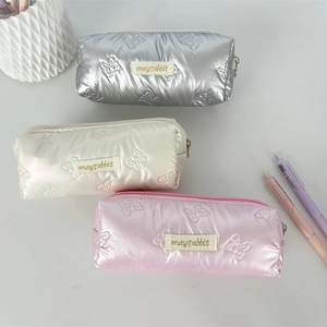 Close-up of quilted bow-patterned pencil cases in silver, white, and pink finishes