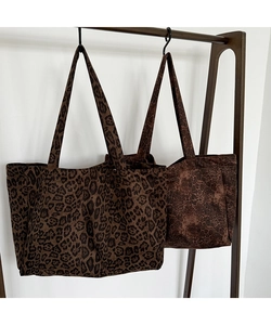 Close-up of two leopard print canvas tote bags hanging on a wooden hook in a minimalist setting