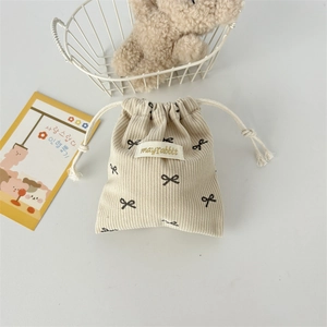 Detailed view of beige corduroy drawstring bag with black bow print and woven label