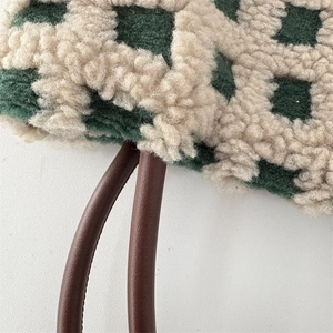 Détail du sac à carreaux en polaire sherpa verte avec poignée en cuir brun et coutures