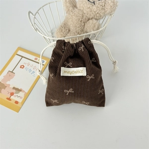 Detail of dark brown corduroy drawstring bag featuring white bow patterns and fabric label