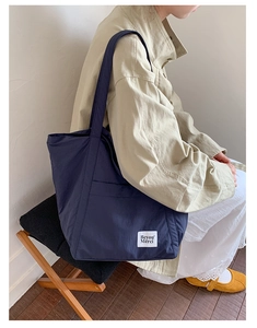 Detail of dark blue nylon tote bag with Beyou Merci label shown on a seated model