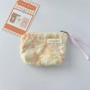 Detailed macro view of yellow floral lace coin purse with pink ribbon zipper and logo patch