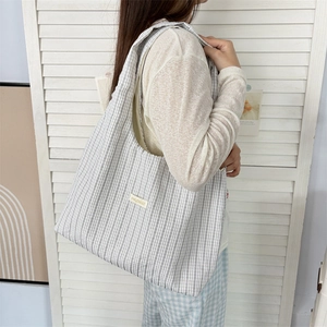 Detail of grey and white striped canvas tote bag with yellow label and wide shoulder strap