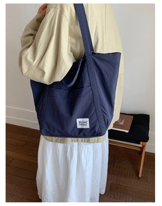 Detail showing the large navy blue nylon tote bag with front pocket and brand label