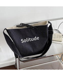 Close-up of black denim tote bag with Solitude print and delicate ribbon bow detail