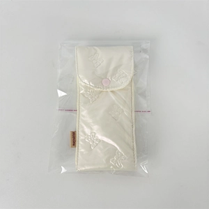 Detail of cream glossy pouch featuring embossed bow patterns and a pink snap button closure