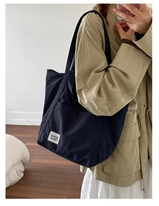 Detail of navy nylon tote bag showing the front pocket and white branded patch design
