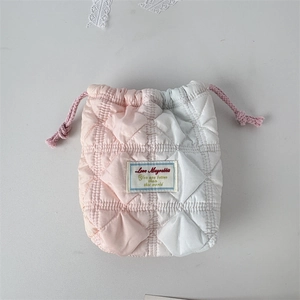 Close-up of quilted two-tone drawstring camera pouch with diamond patterns and woven label
