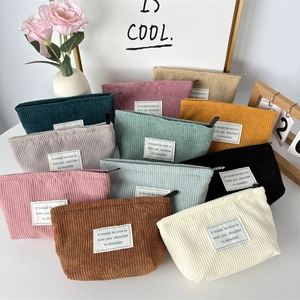 Stack of colorful corduroy makeup bags with metal zippers and woven labels in minimalist decor