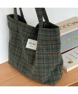 Close-up of a green plaid tote bag with hand-made label on a natural wooden table