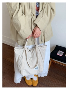 Detail view of a large beige nylon tote bag worn by a model in casual spring outfit