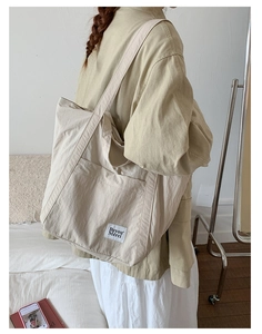 Detail of a beige nylon tote bag with a small woven label and front pocket design