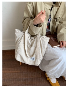 Detail of minimalist beige nylon tote bag with functional front pockets and brand label