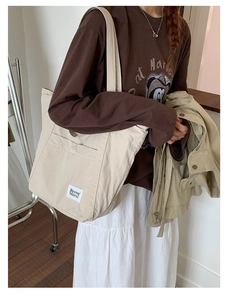 Detail view of large beige nylon tote bag with pocket worn with a casual commute outfit
