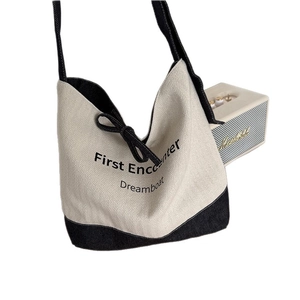 Minimalist canvas bucket tote bag in beige and black with First Encounter slogan and bow