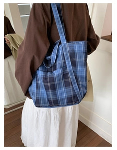Detail of blue plaid canvas tote bag showing side pocket and thick shoulder strap