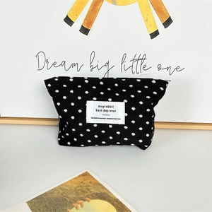 Detailed view of black polka dot corduroy makeup bag with woven brand label on surface