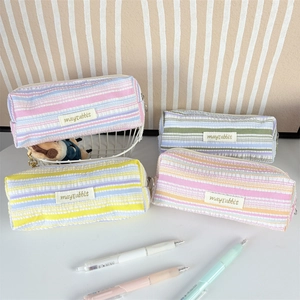 Minimalist striped seersucker pencil cases in assorted pastel colors on a white desk