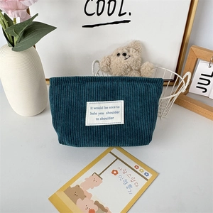 Close-up of dark teal corduroy makeup bag with textured vertical stripes and canvas patch