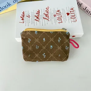 Détail du porte-monnaie en velours côtelé fleuri avec zip jaune et dragonne rose