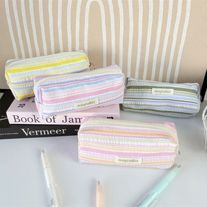 Close-up of four pleated striped pencil cases with metal zippers and woven labels