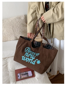 Detail of brown corduroy tote bag with blue Brave new world embroidery and plaid lining