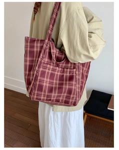 Deep red vintage plaid canvas tote bag worn by a model in a minimalist indoor setting