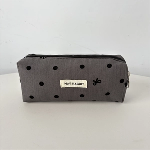 Detailed shot of dark gray corduroy makeup bag with black polka dots and zipper