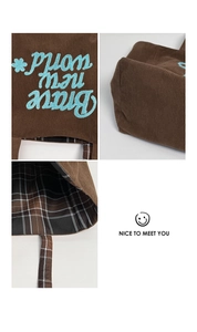 Detail of brown corduroy tote with Brave new world embroidery and plaid lining