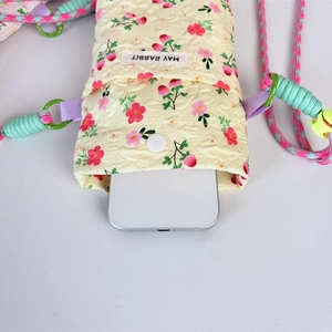 Detail showing a quilted floral phone bag with a magnetic snap button and woven shoulder strap