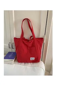 Detail of red nylon tote bag with brand label and front pocket on white sofa