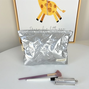 Silver quilted makeup bag with bow pattern and metal zipper on a white vanity desk