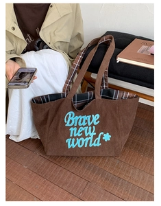 Detailed close-up of brown corduroy tote bag with blue embroidered text and plaid lining