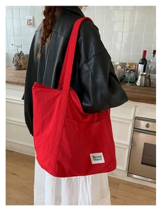 Close-up of a red nylon tote bag with white logo patch and shoulder strap detail