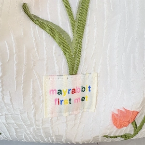 Detail aus weißem Jacquard-Stoff mit Tulpen-Stickerei und Mayrabbit-Aufnäher-Etikett