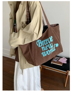 Close-up of brown corduroy tote bag with blue embroidered text and plaid lining